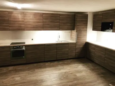 Même pièce après travaux : cuisine équipée en bois foncé, plan de travail blanc et four encastré